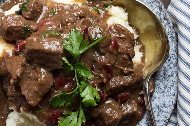 braised beef with cranberries on plate with mashed potatoes