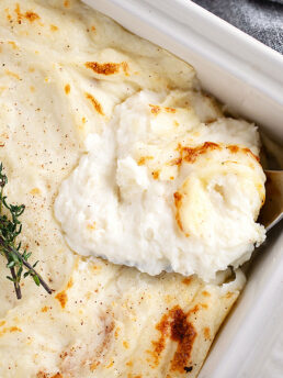 Make-ahead mashed potatoes in a casserole dish being spooned out.