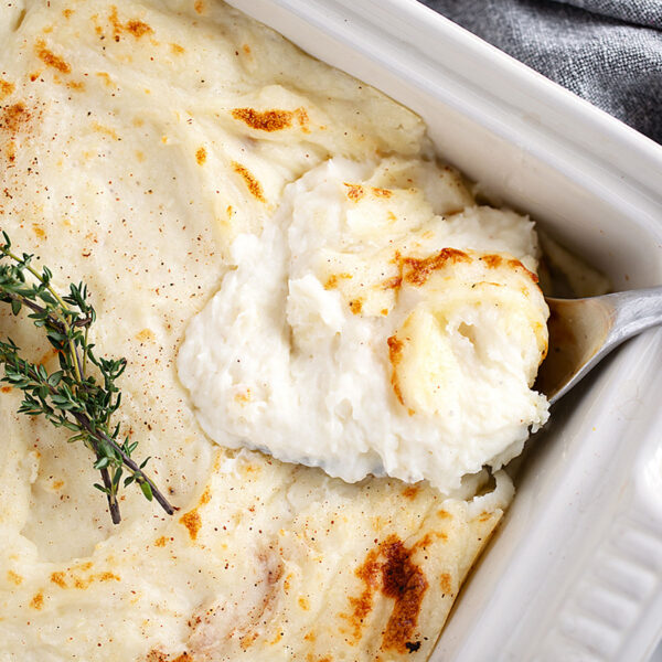 Make-ahead mashed potatoes in a casserole dish being spooned out.