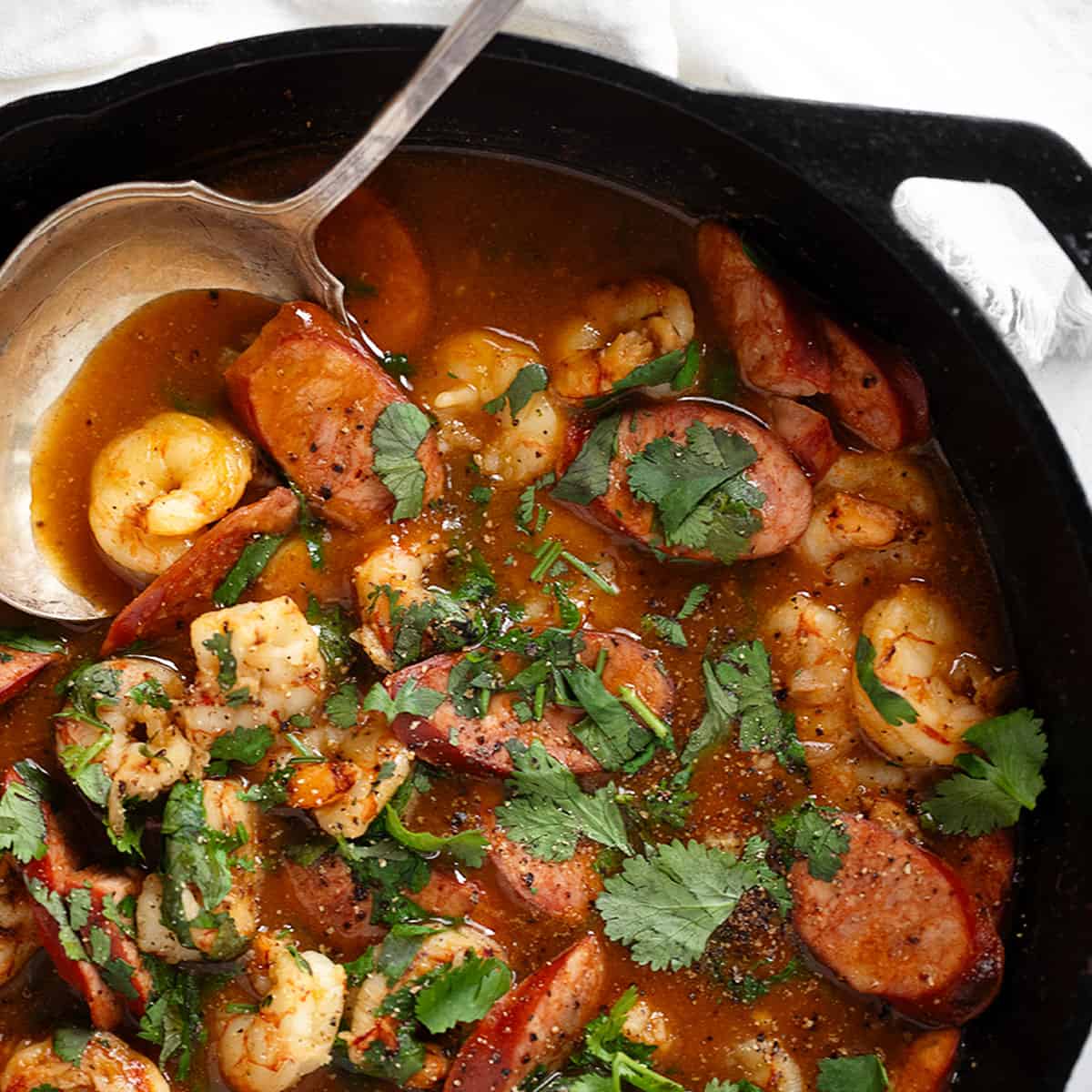 Spicy sausage and shrimp in a cast iron skillet with spoon.