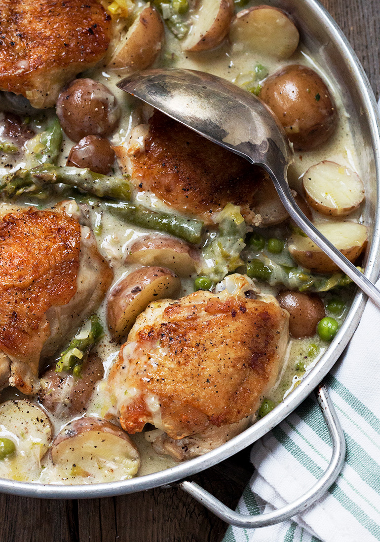 Creamy chicken thighs and asparagus in skillet with potatoes and peas.