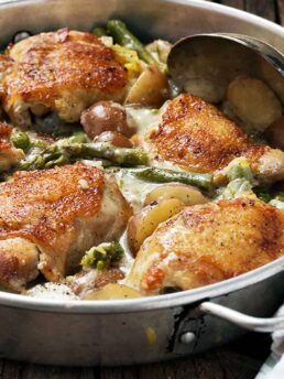 Creamy chicken thighs, asparagus and potatoes in a serving dish.