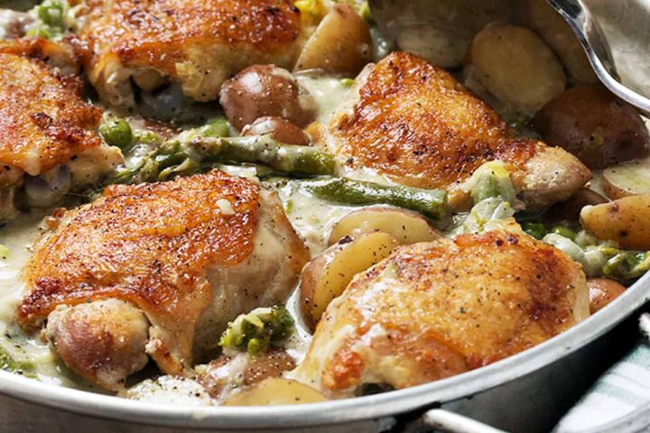 Creamy chicken thighs, asparagus and potatoes in a serving dish.