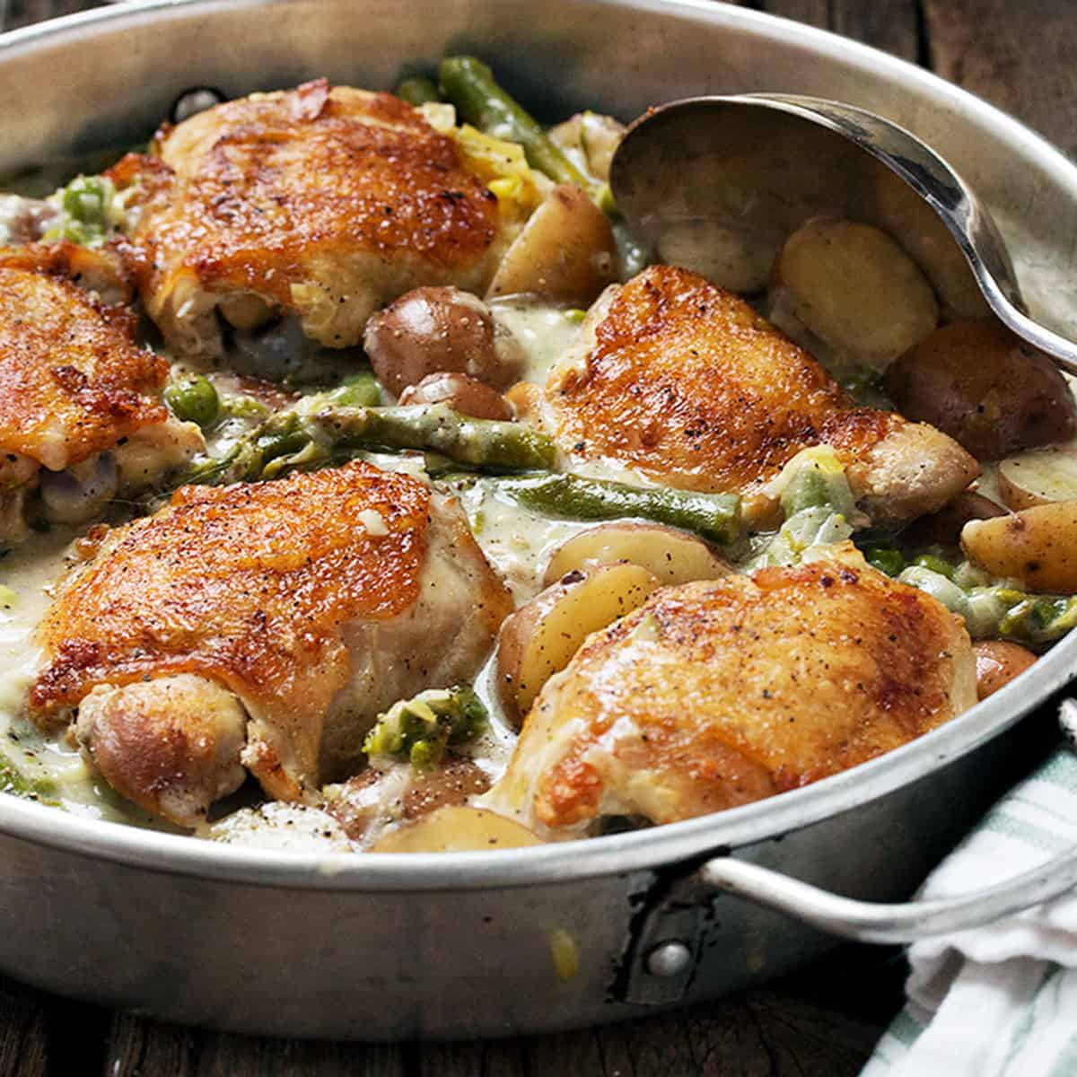 Creamy chicken thighs, asparagus and potatoes in a serving dish.