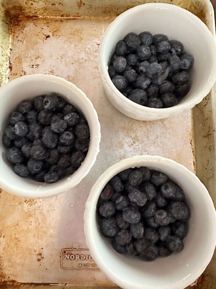 Blueberries in ramekins on a baking sheet.