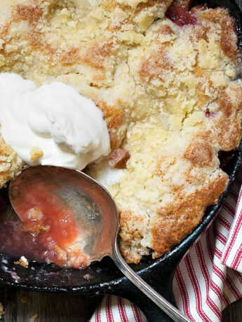 strawberry rhubarb cobbler in cast iron skillet with spoon