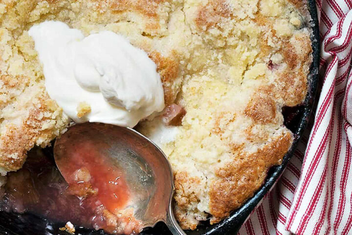 strawberry rhubarb cobbler in cast iron skillet with spoon