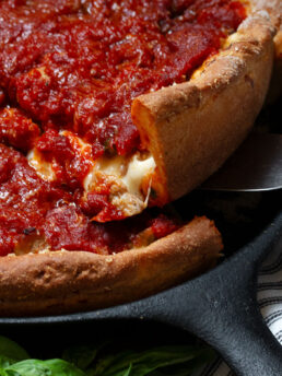Chicago style deep dish pizza in a cast iron skillet lifting a slice out of the pan.