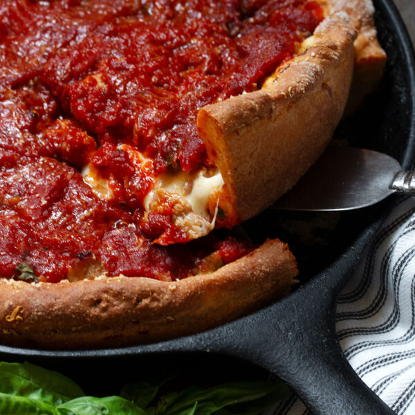 Chicago style deep dish pizza in a cast iron skillet lifting a slice out of the pan.