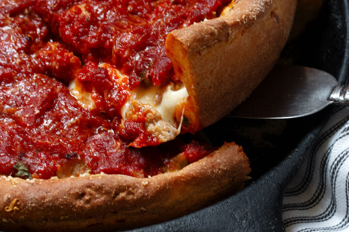 Chicago style deep dish pizza in a cast iron skillet lifting a slice out of the pan.