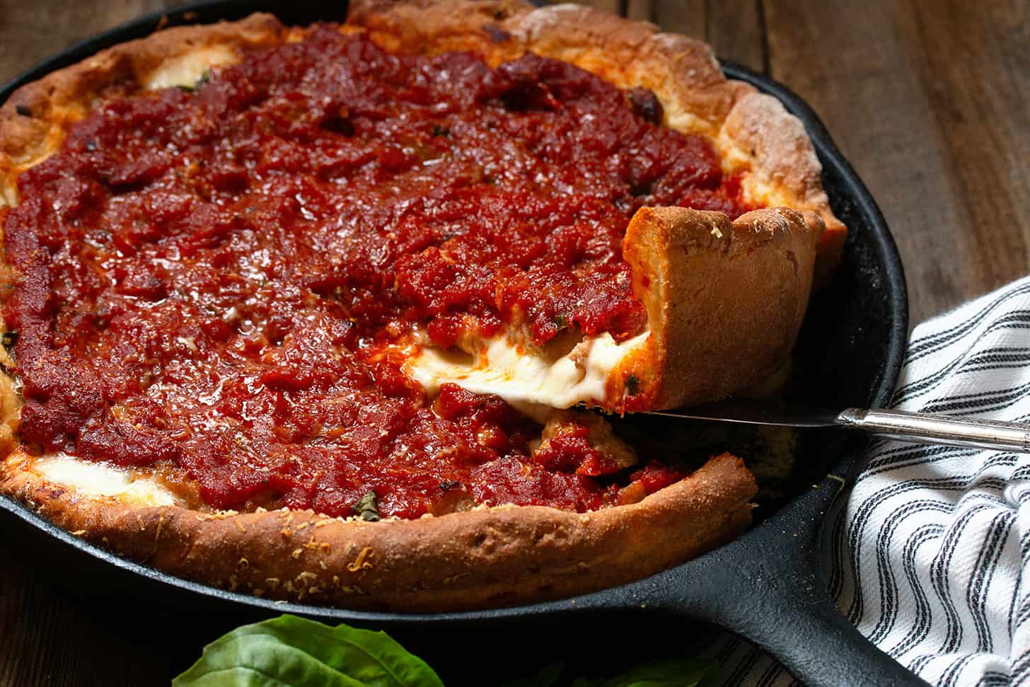 Lifting a slice of Chicago style deep dish pizza in a cast iron skillet.