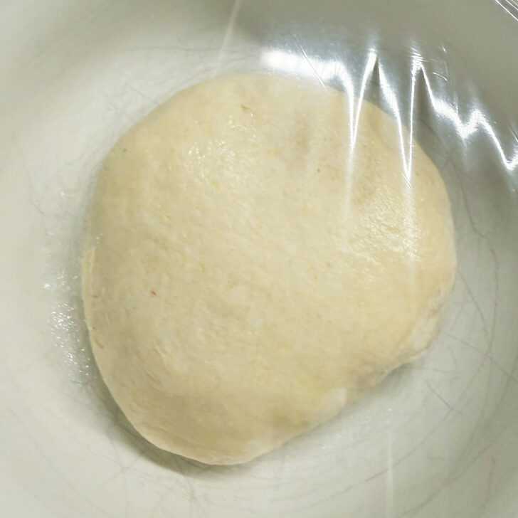 Deep dish pizza dough in a plastic-covered bowl to rise.