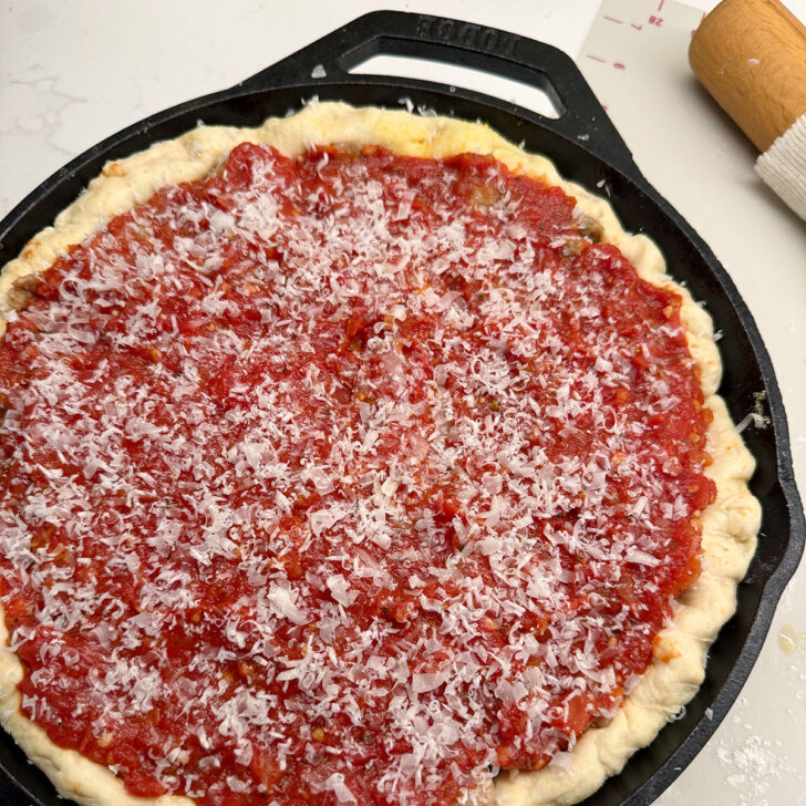 Pizza sauce and Parmesan topping added to the deep dish pizza.