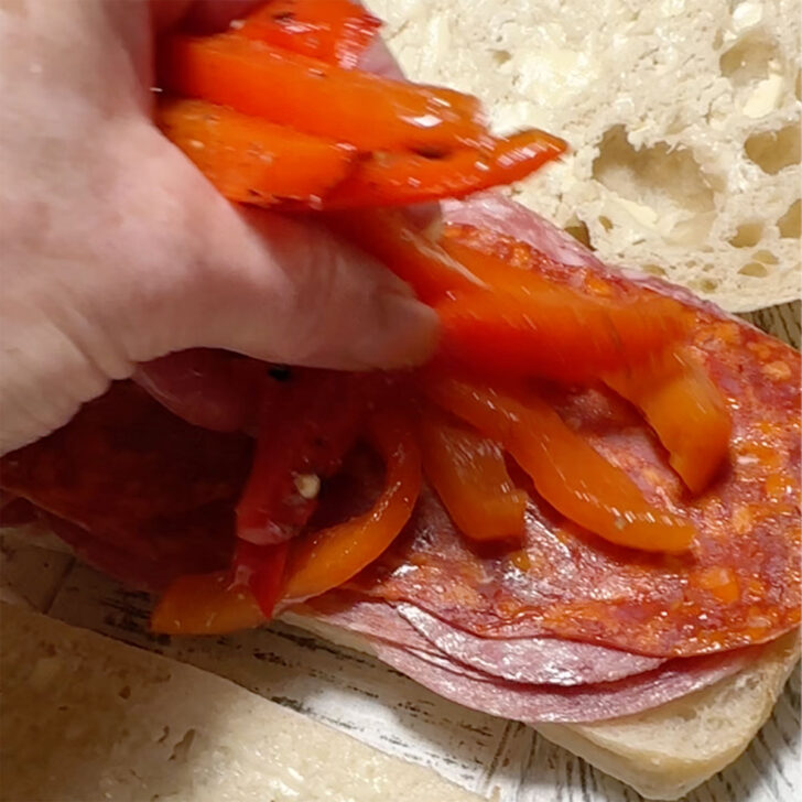 Adding the roasted red peppers to the sandwich.
