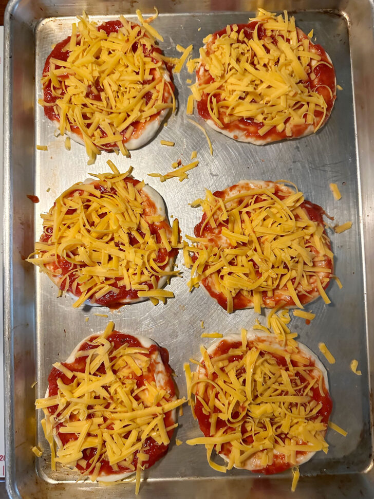 Pizza buns topped with pizza sauce and cheese.