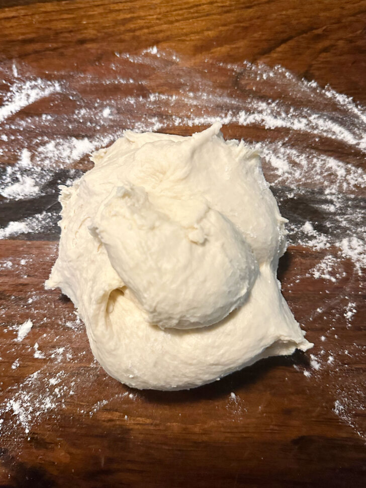 Finished pizza buns dough on a floured counter.