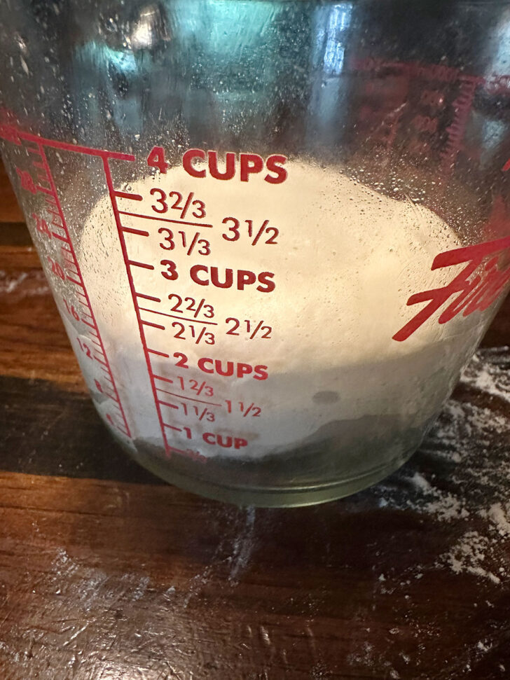 Pizza buns dough set into a large measuring cup to rise.