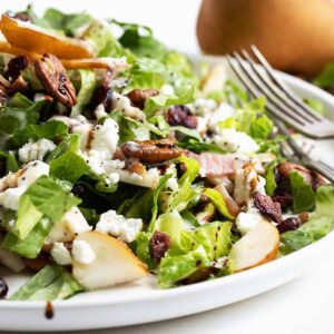 Fall pear chopped salad on white plate with pear behind