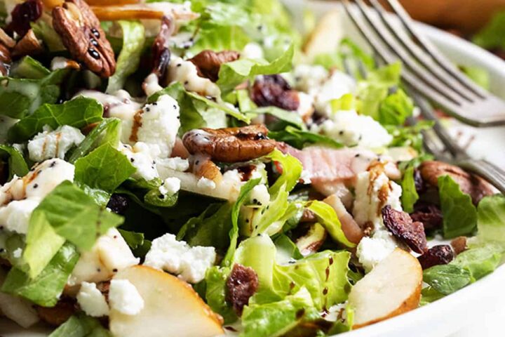 Fall pear chopped salad on white plate with pear behind