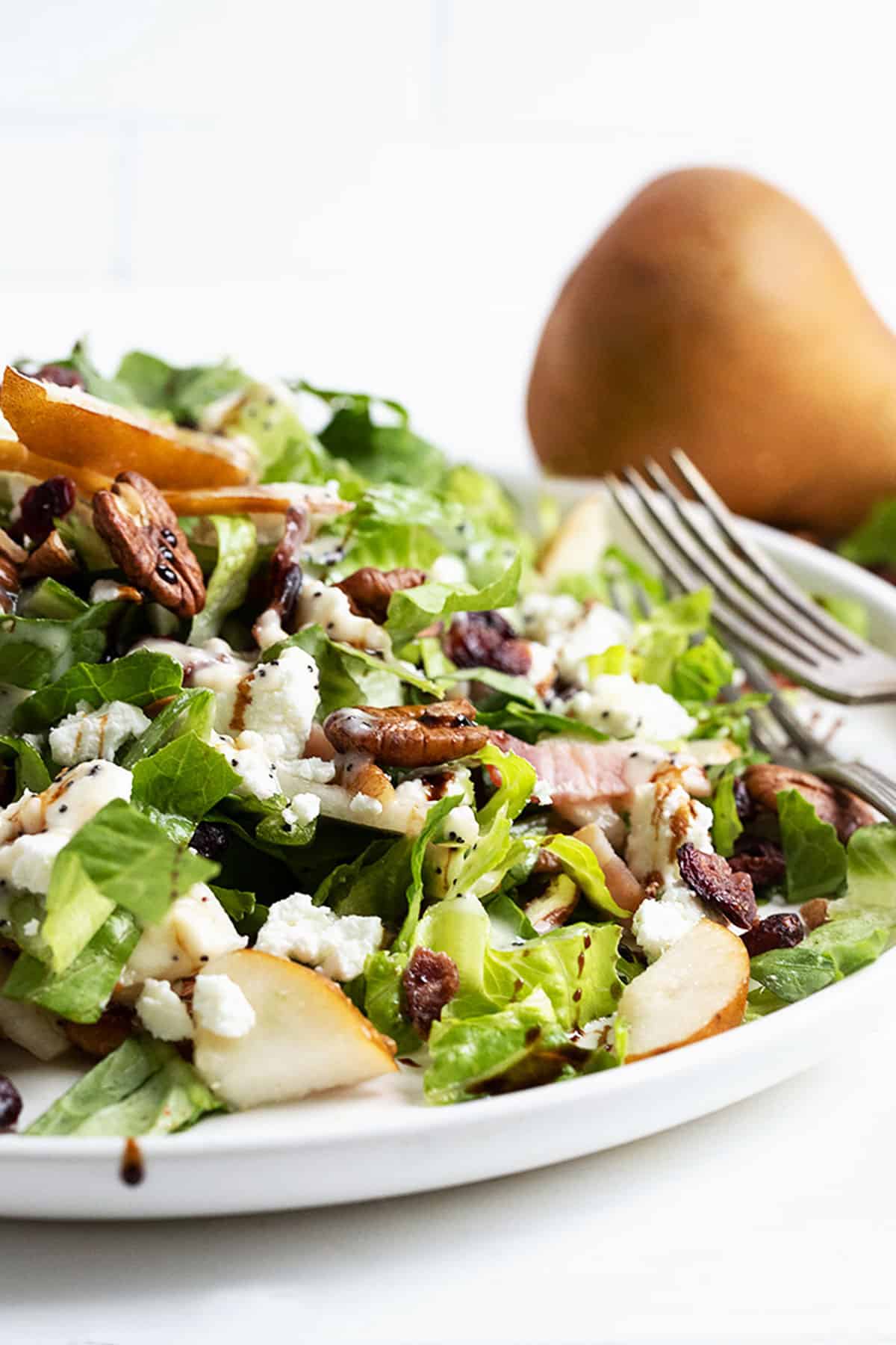 Fall pear chopped salad on white plate with pear behind