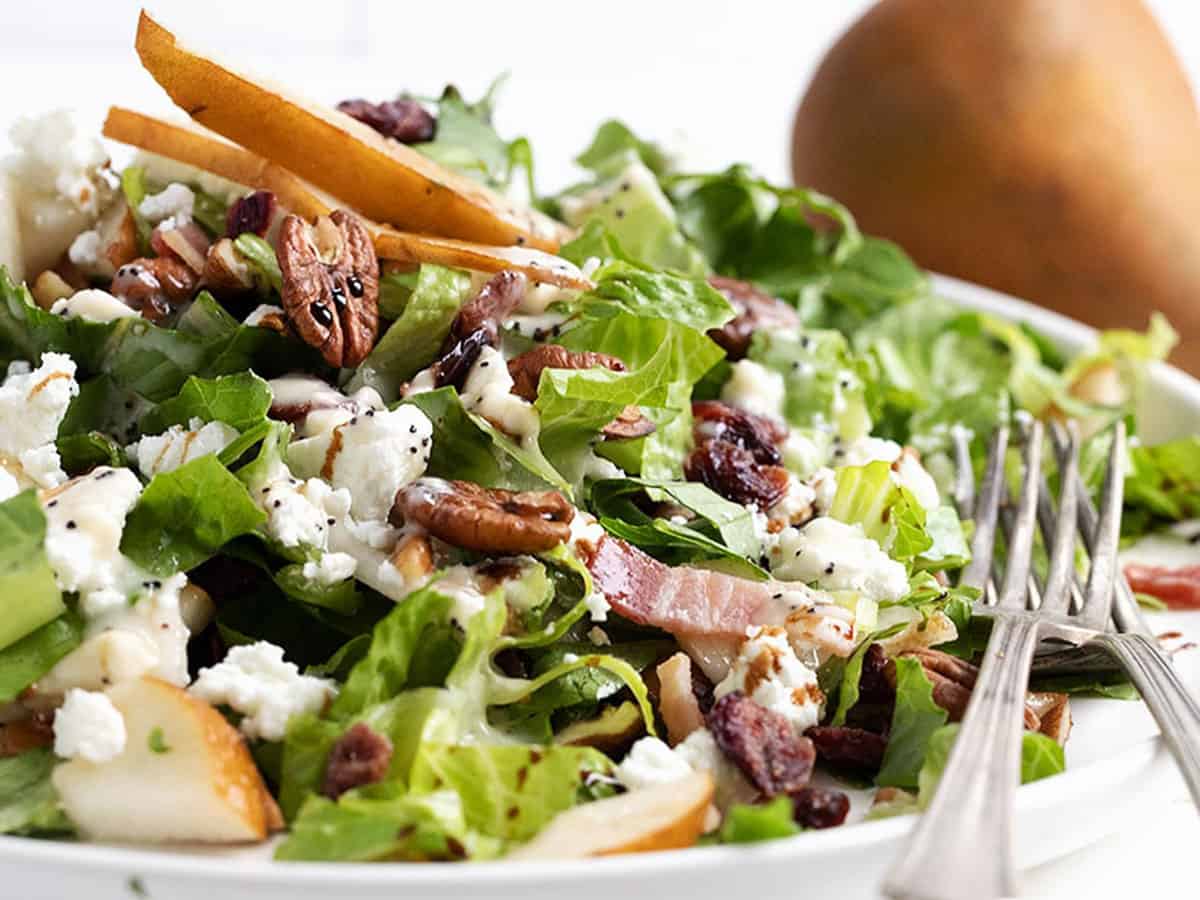 Fall pear chopped salad on white plate with pear behind