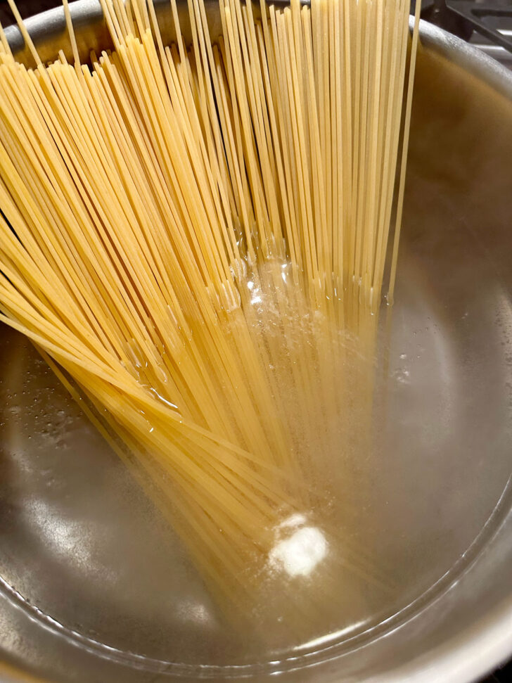 Adding dried spaghetti to boiling water.