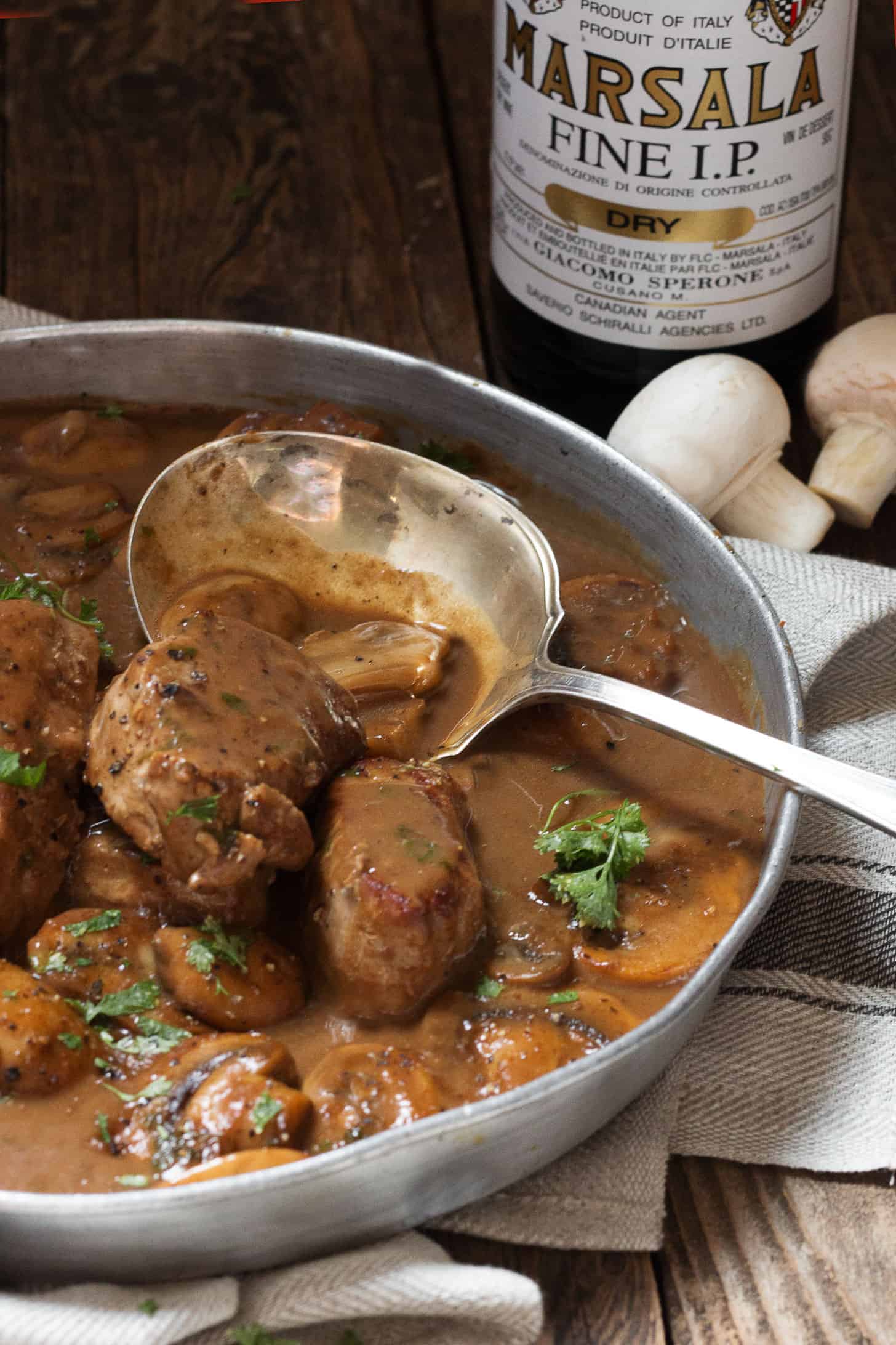 Pork Marsala with mushrooms in a serving dish with a spoon.