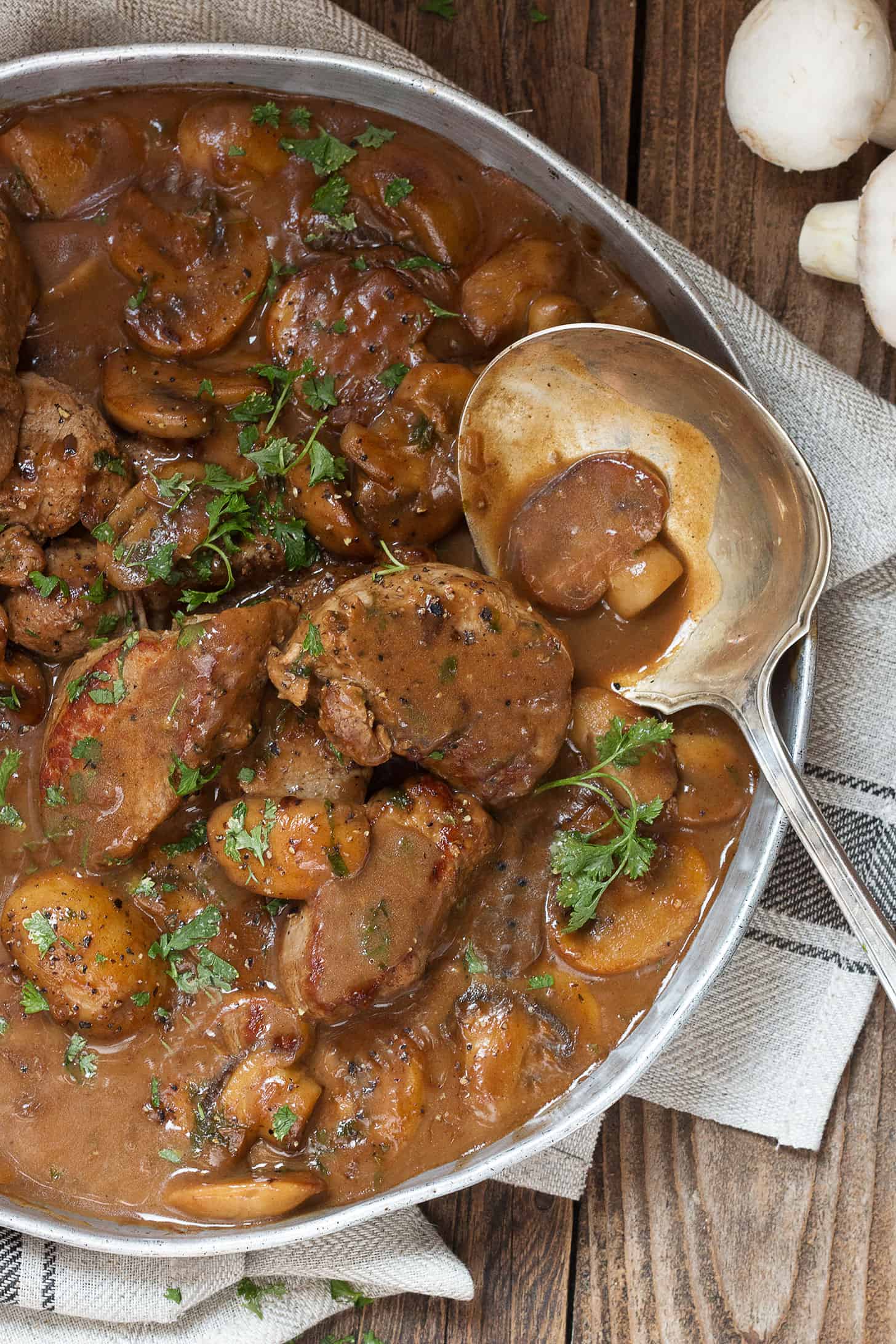Pork Marsala with mushrooms in a serving dish with a spoon.