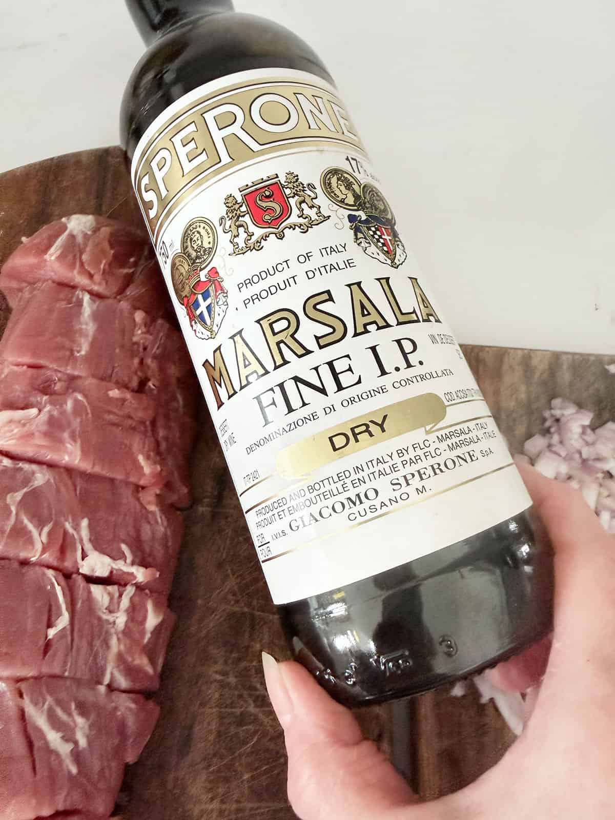 Marsala wine bottle next to pork tenderloin.