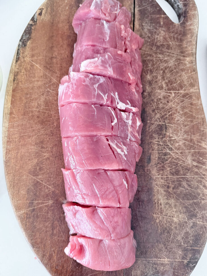 Pork tenderloin cut into slices on a cutting board.