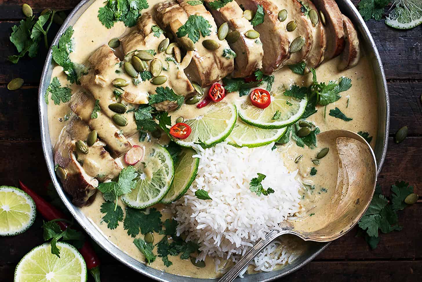 Thai green curry pork tenderloin on platter with limes and rice