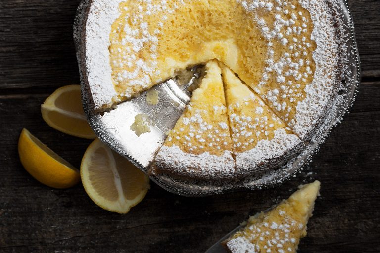 Top down view of icing sugar dusted Lemon Cream Butter Cake with a slice removed