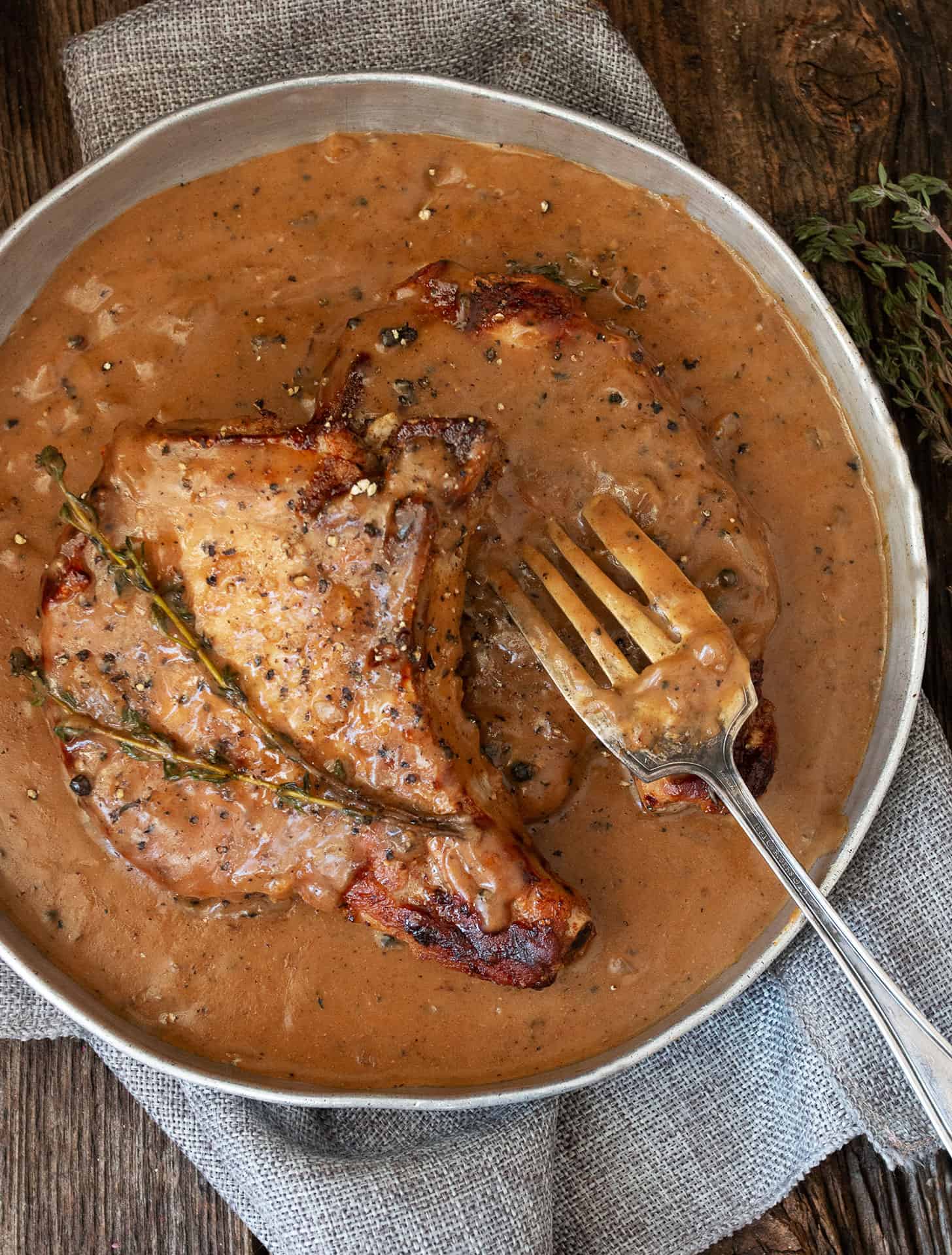 pork chops with peppercorn sauce in serving dish with fork