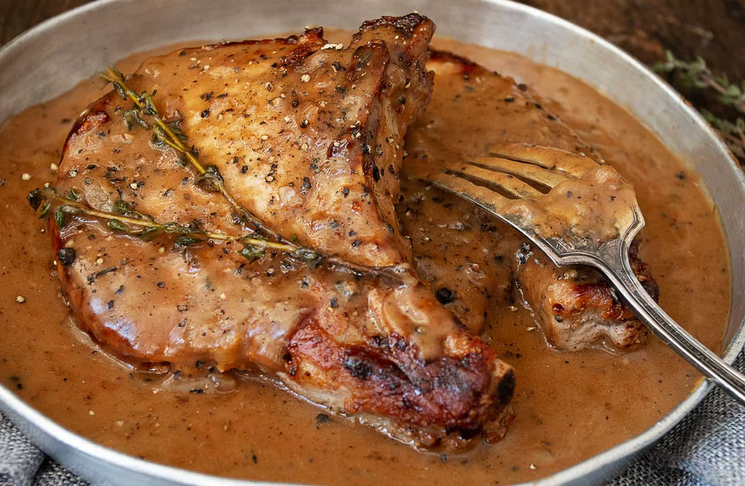 pork chops with peppercorn sauce in serving dish with fork