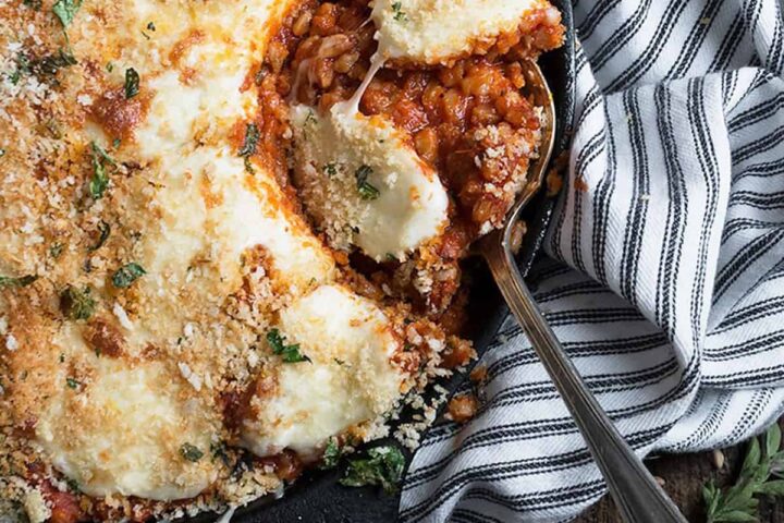 sausage and farro baked in tomato sauce and topped with cheese in skillet with spoon