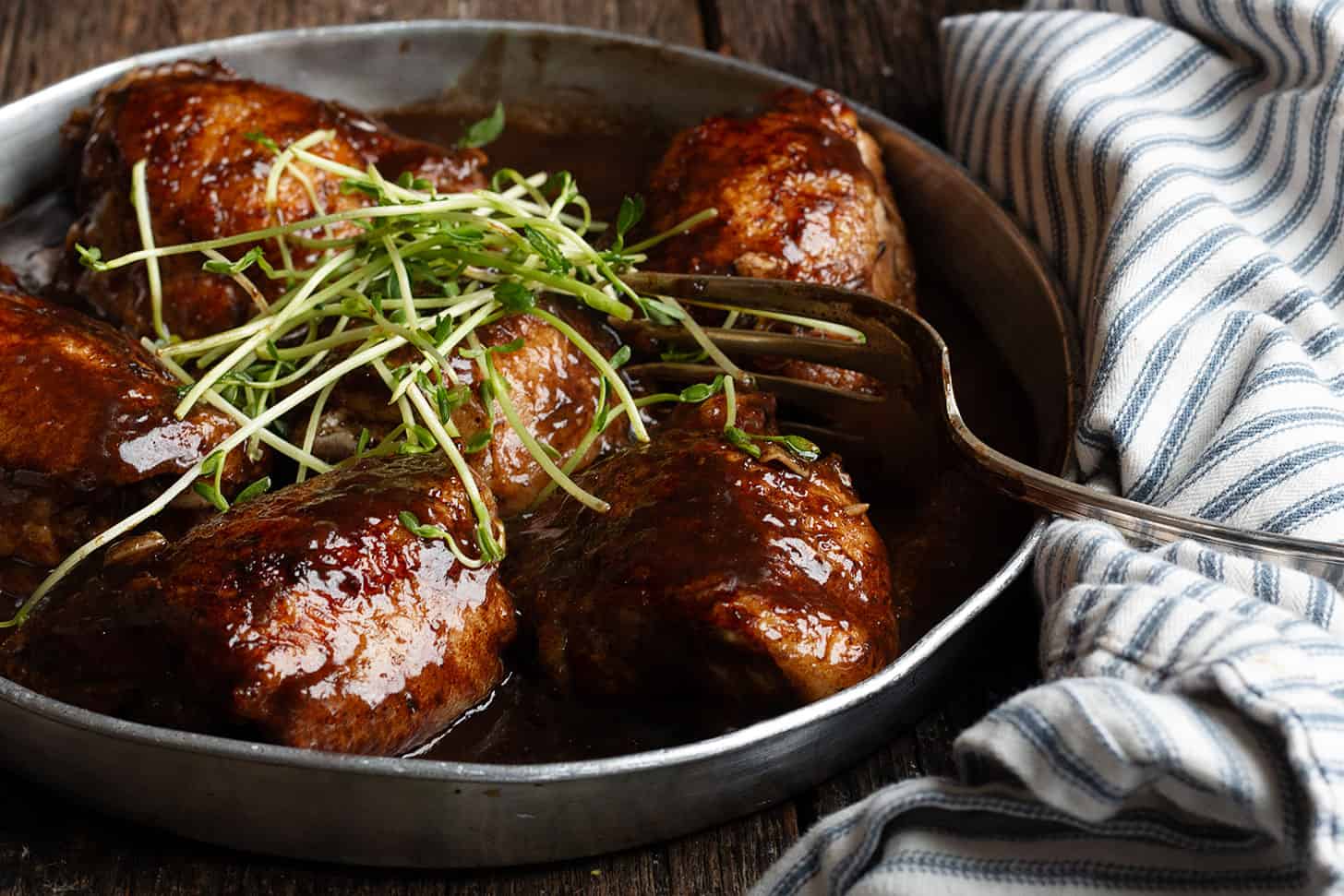 Balsamic chicken thighs in serving dish with fork.