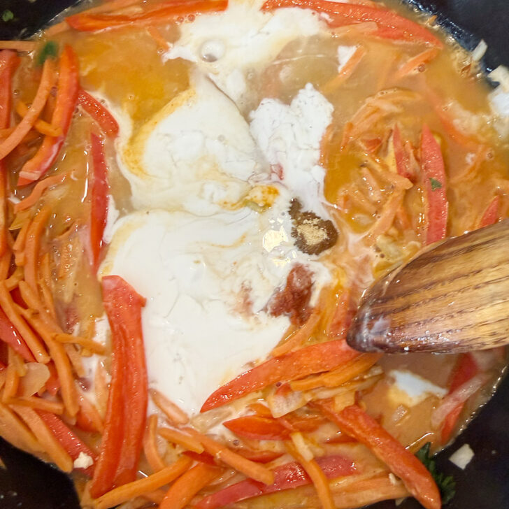 Adding coconut milk and Thai red curry paste to the skillet with the vegetables.