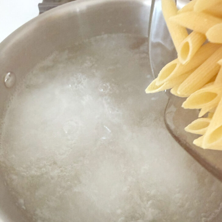 Adding penne pasta to boiling water.