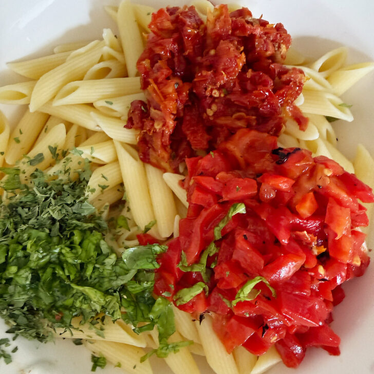 Sun-dried tomatoes, roasted red peppers and parsley added to the pasta in the bowl.