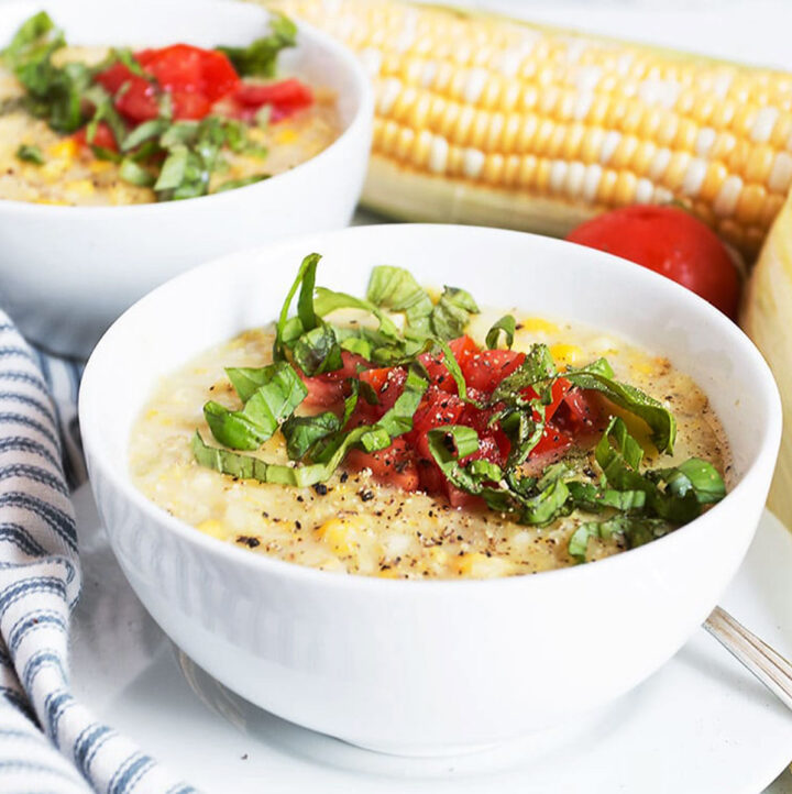 fresh corn soup in white bowls with basil and tomatoes on top