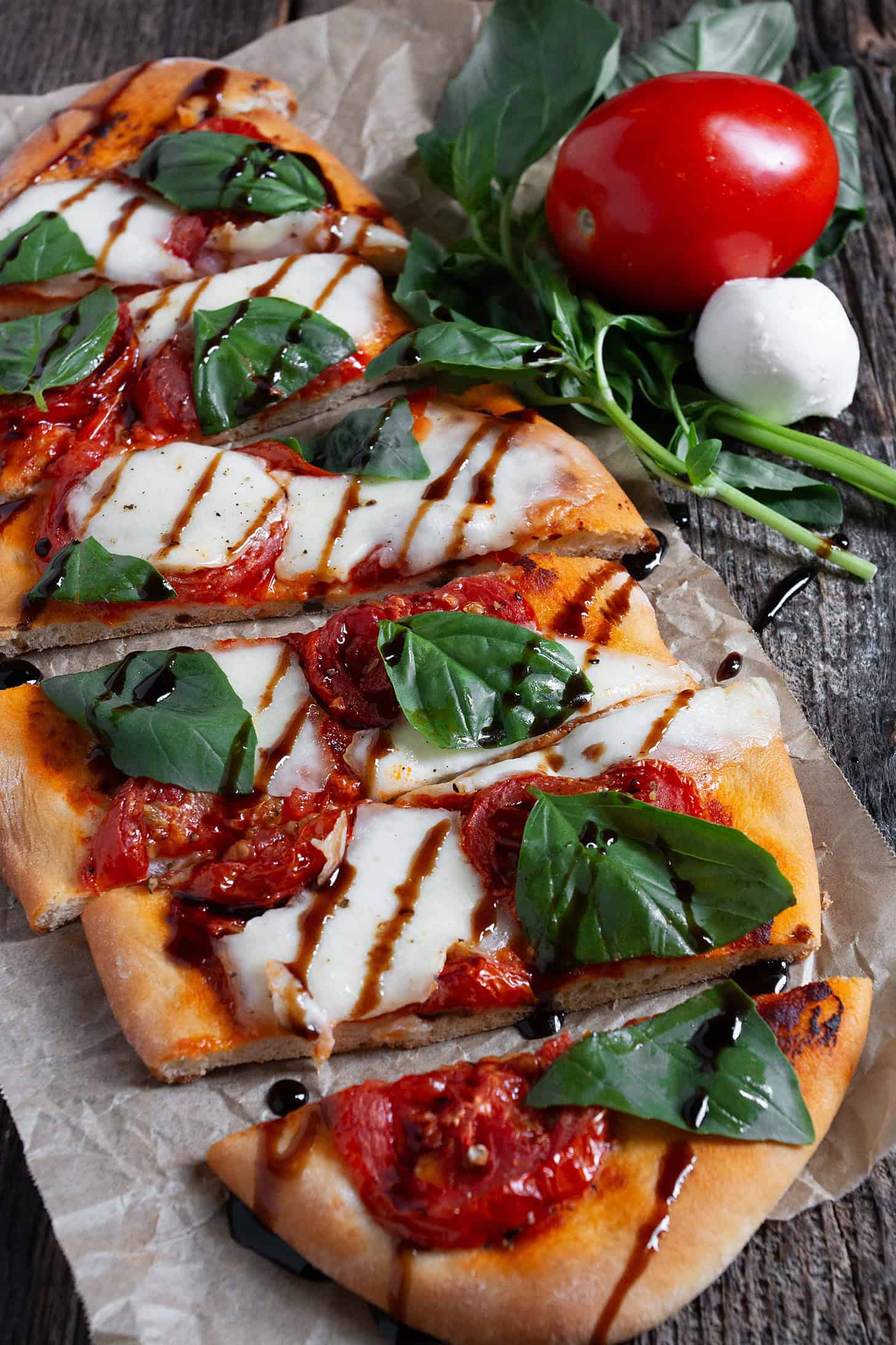 Tomato bocconcini flatbread sliced on parchment paper.
