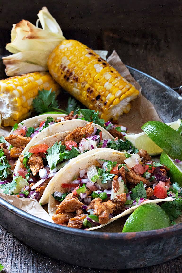 tacos al pastor on platter with lime slices