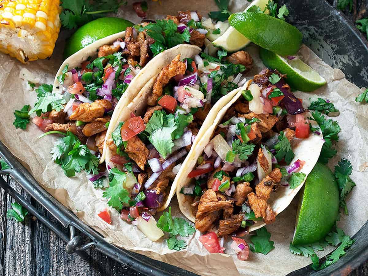 tacos al pastor on platter with lime slices