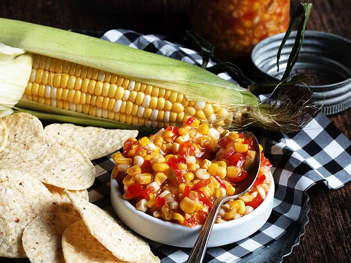 corn and chile salsa in small bowl with tortilla chips and corn in the background