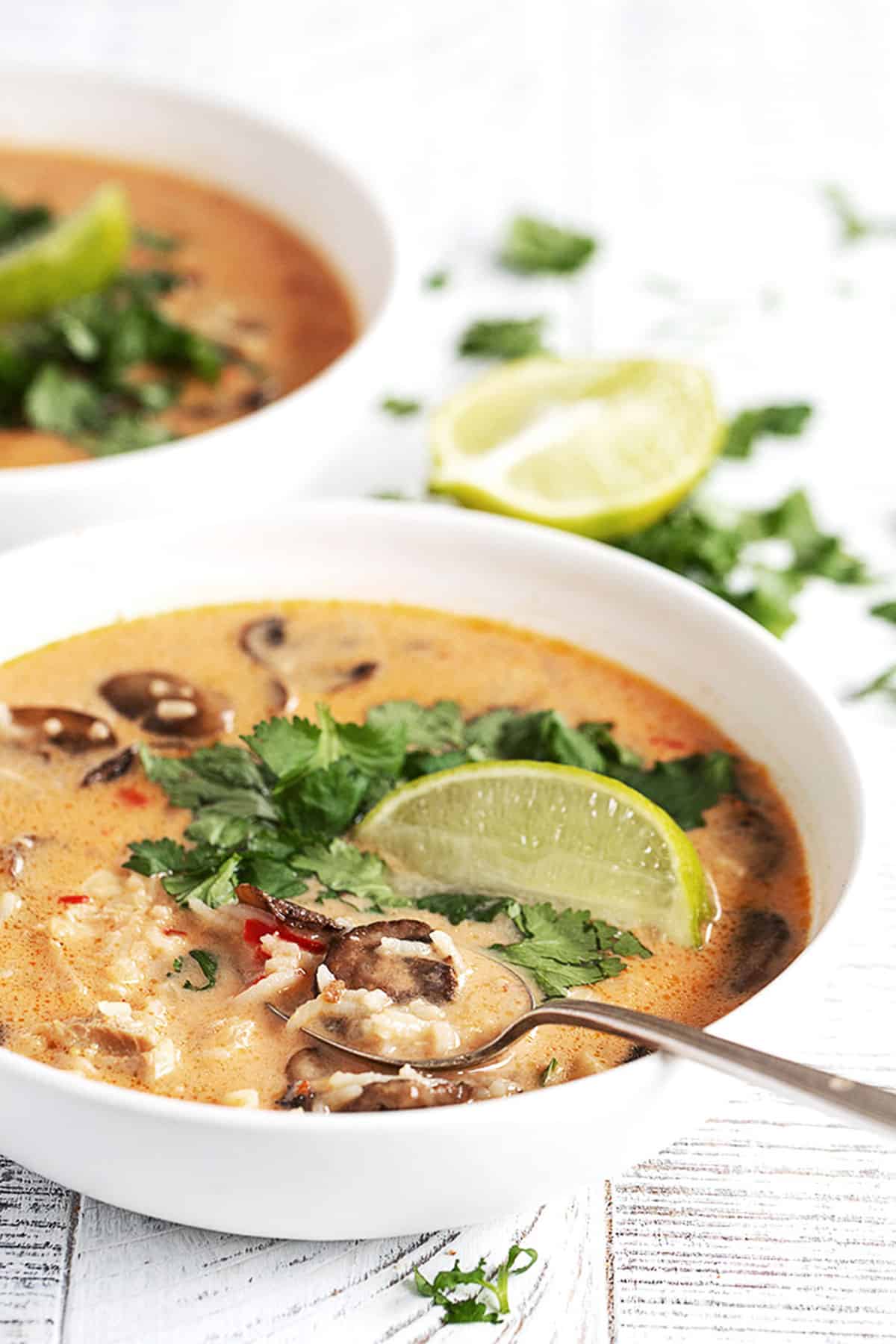 Wicked Thai chicken soup in white bowl with limes and cilantro