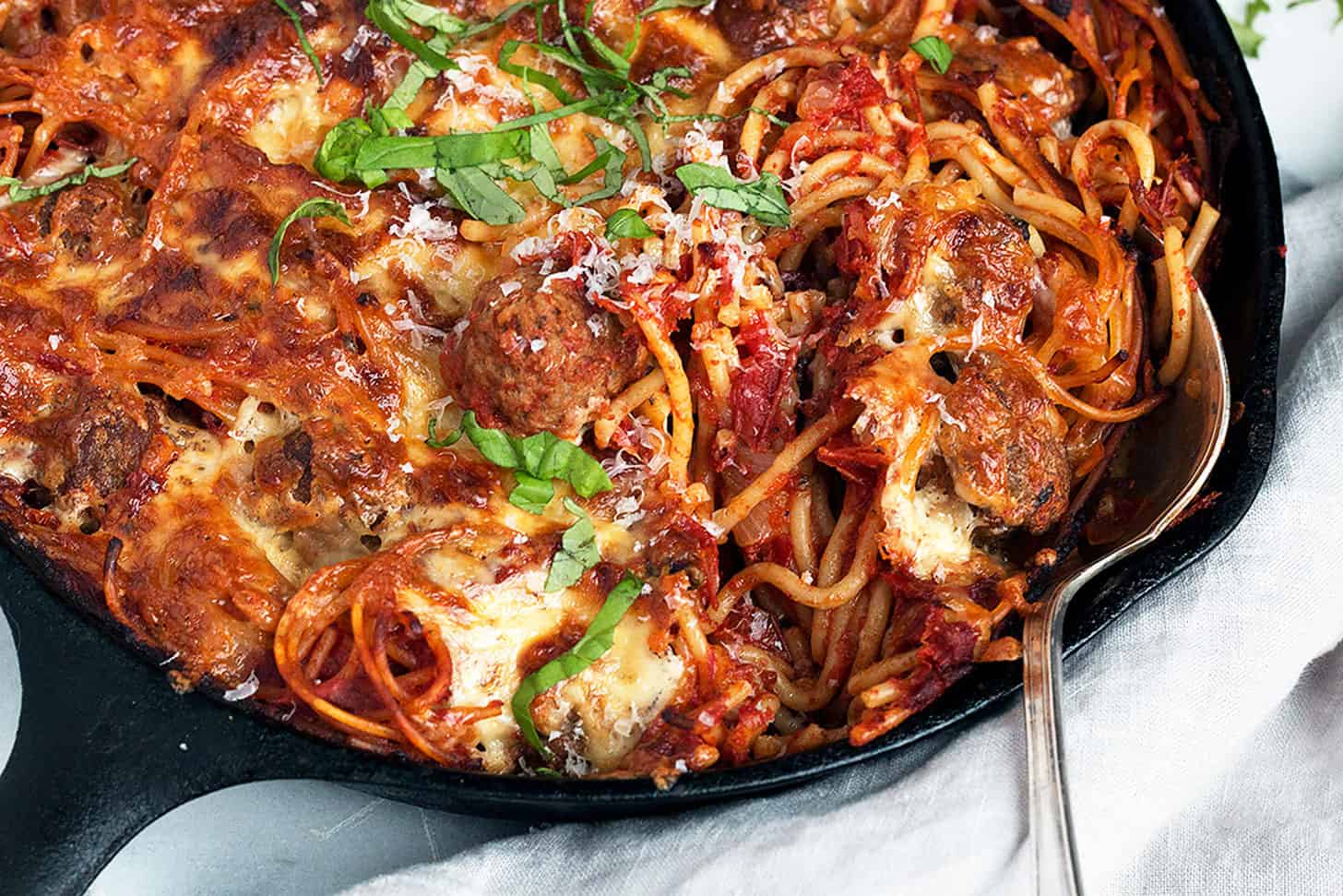 baked spaghetti and meatballs in cast iron skillet with spoon