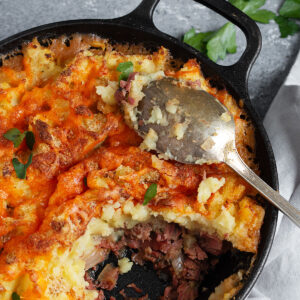 Corned beef cottage pie in skillet with a spoon.