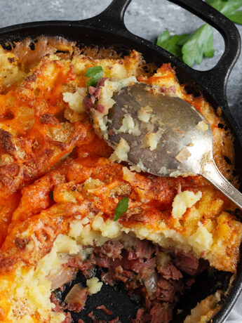 Corned beef cottage pie in skillet with a spoon.