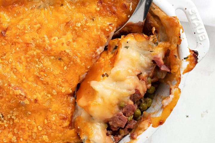 Corned beef cottage pie in cooking dish with spoon.