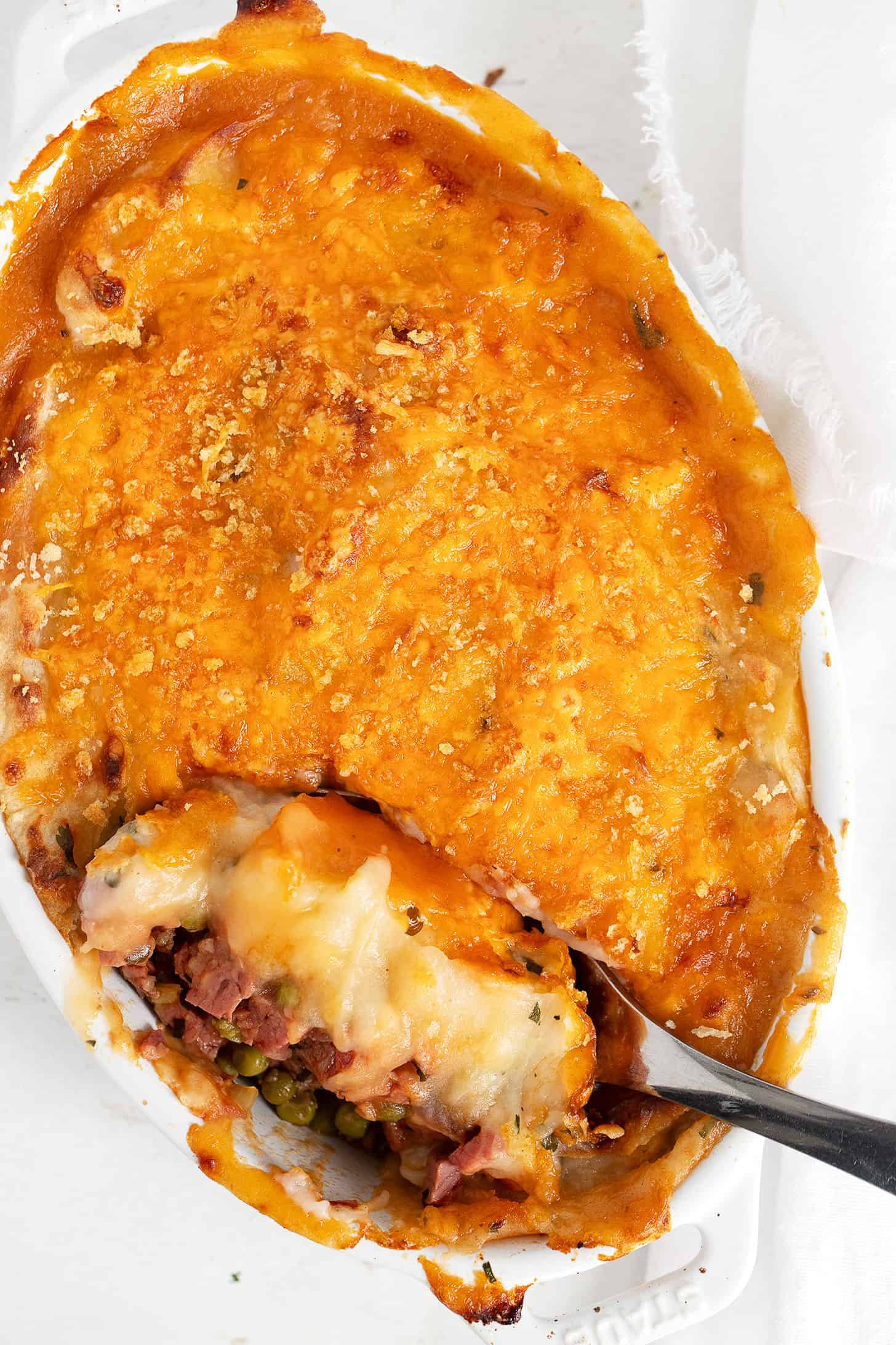 Corned beef cottage pie in cooking dish with spoon.